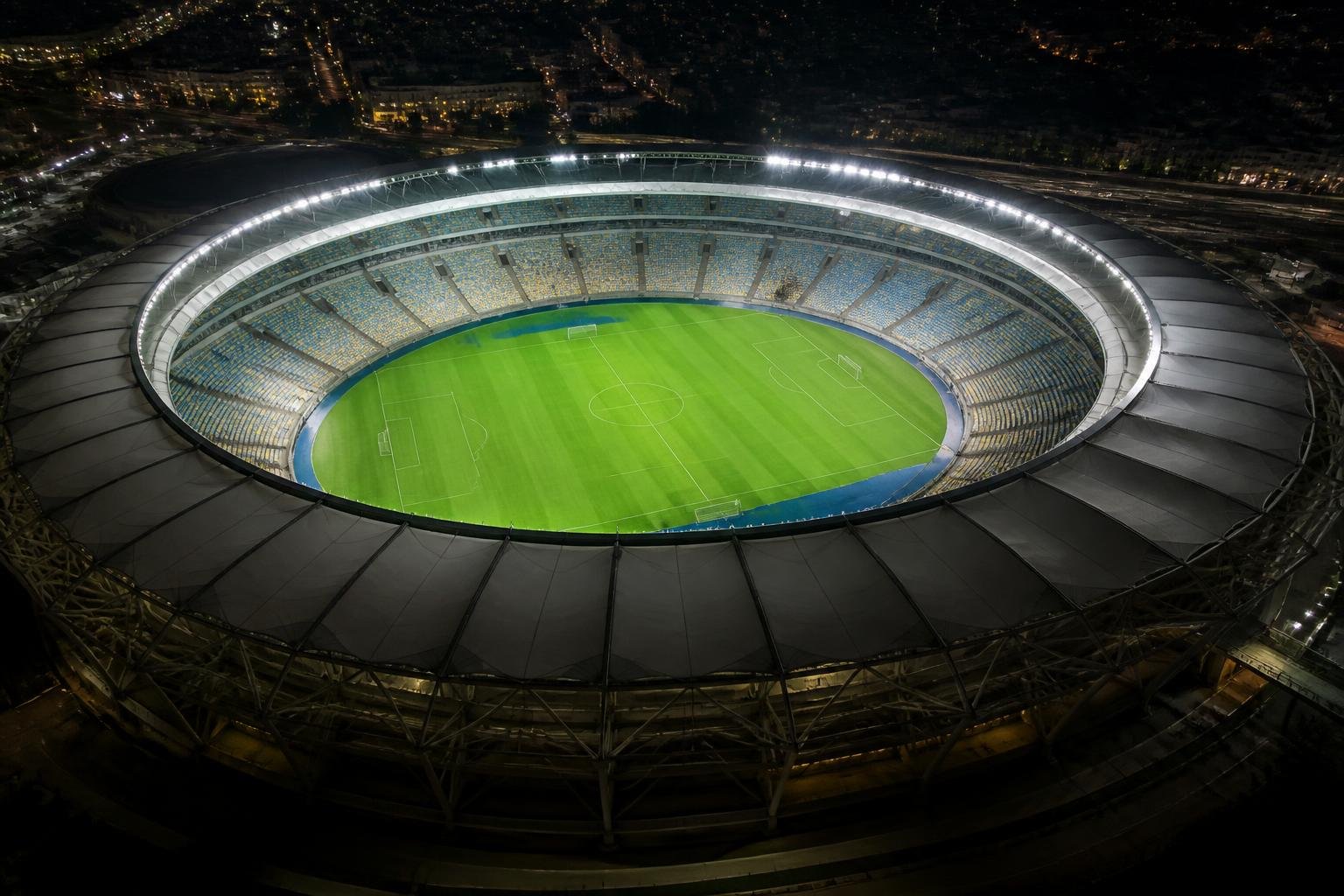 Vista noturna do estádio do Maracanã iluminado, com o gramado vazio e as arquibancadas ao fundo
