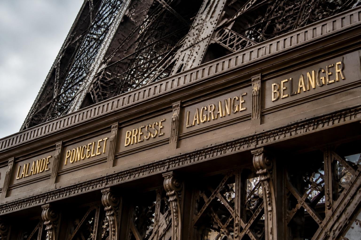 Letras douradas em relevo com sobrenomes gravados na faixa do primeiro andar da Torre Eiffel
